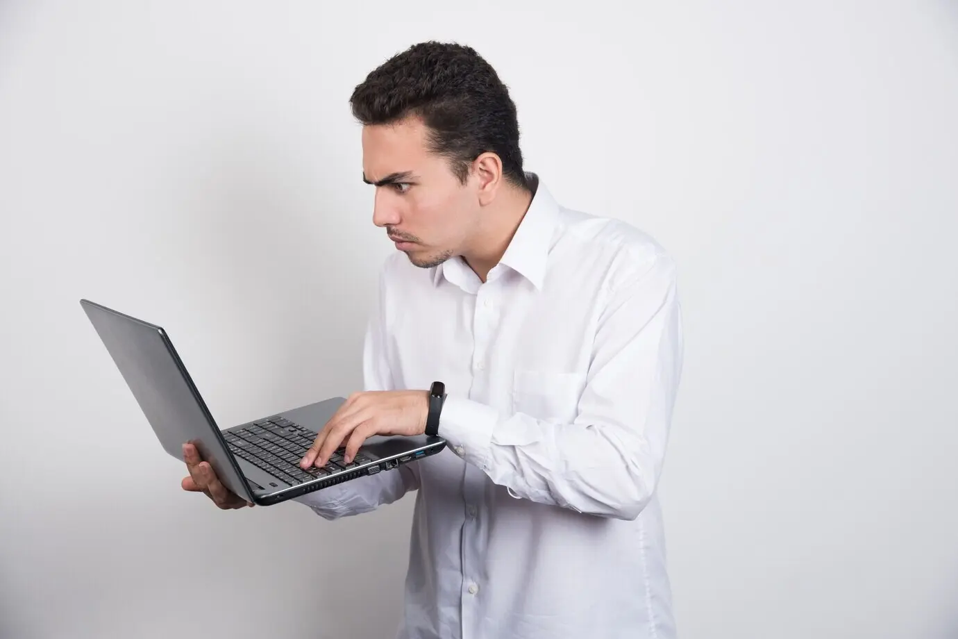 Geschäftsmann schaut intensiv auf einen Laptop vor weißem Hintergrund.